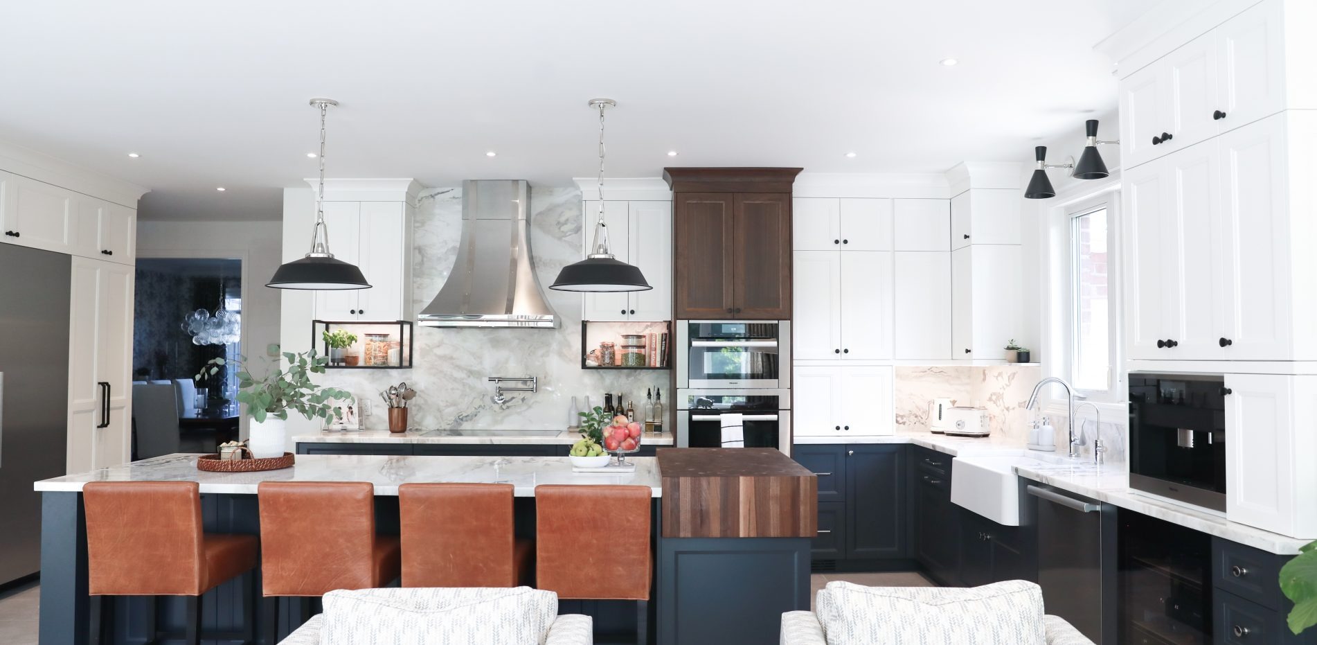 Modern kitchen with white and dark cabinetry, marble countertops, stainless steel appliances, and four brown leather bar stools at the island.