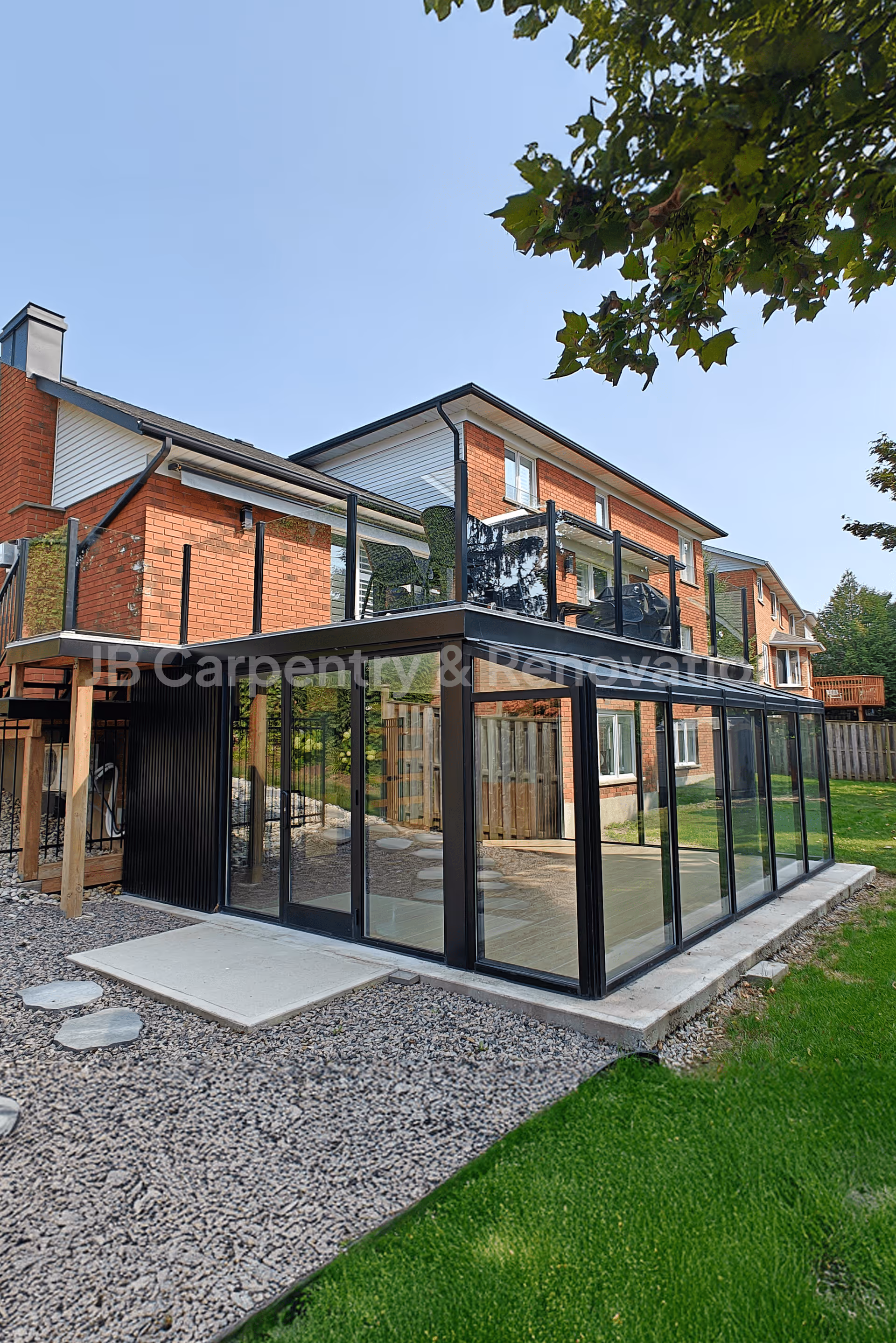 Custom home renovation featuring a modern glass sunroom addition and upper-level deck with black railing — precision exterior carpentry and renovation by JB Carpentry.