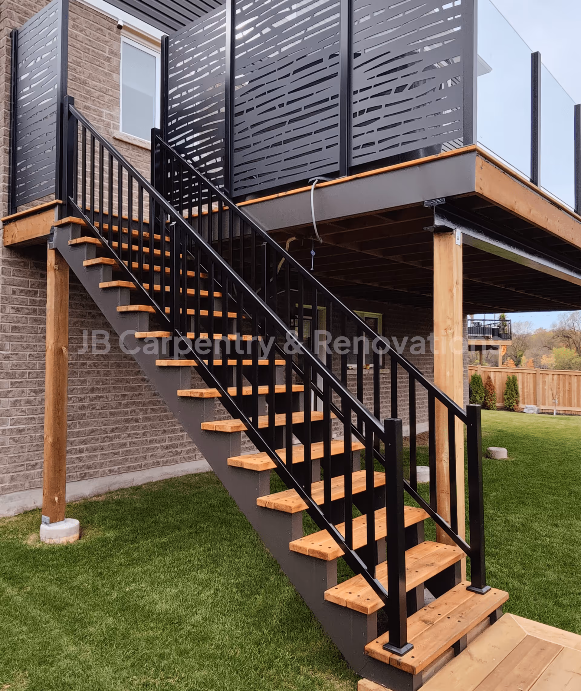 Custom exterior staircase with wood steps and black metal railing leading to a modern deck with privacy panels — designed and built by JB Carpentry & Renovations.