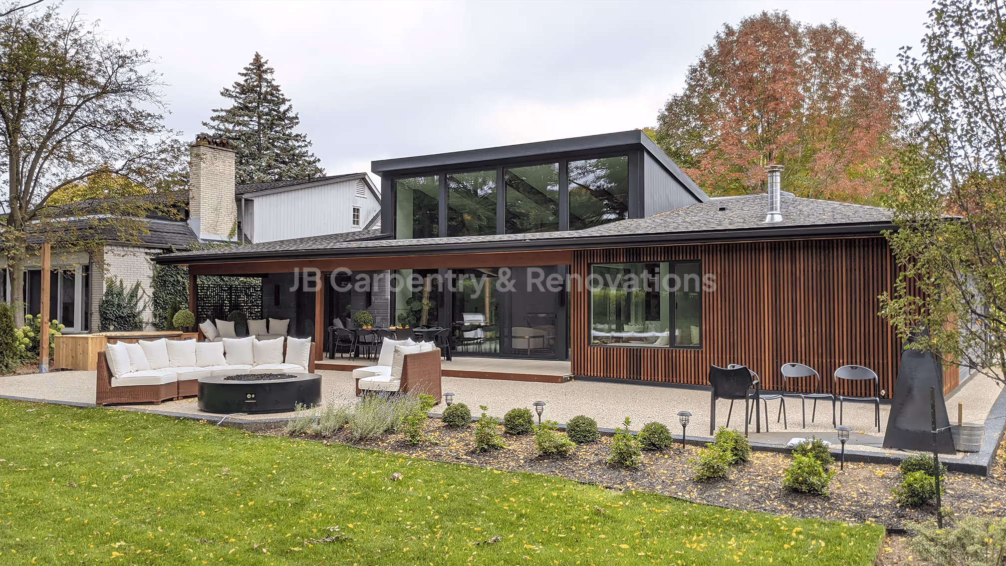 Contemporary home renovation featuring custom wood slat siding, large glass windows, and an outdoor living area — designed and built by JB Carpentry & Renovations.