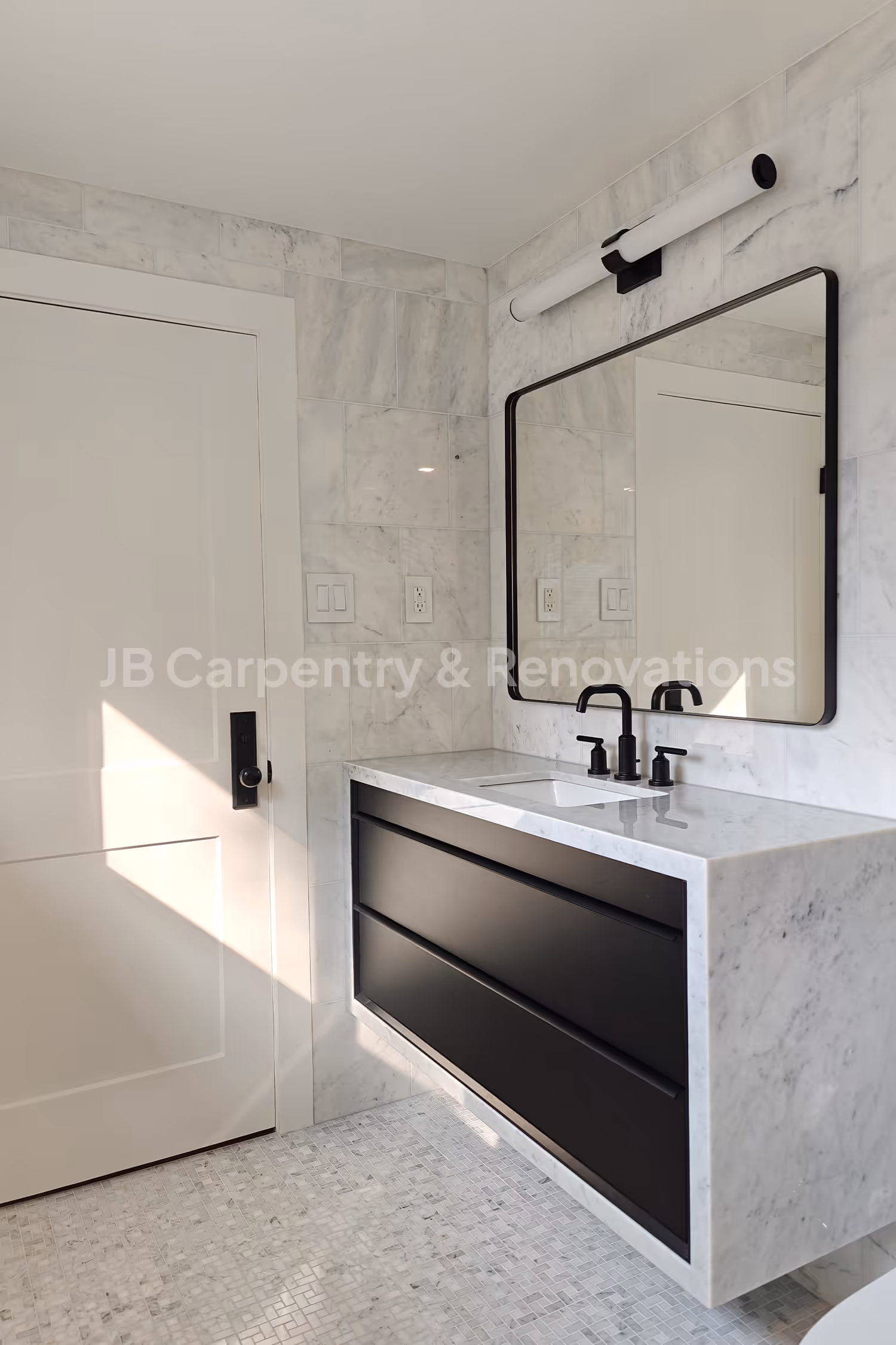 Modern bathroom renovation featuring a custom floating vanity with black drawers, marble countertop, and matching tile walls — designed and built by JB Carpentry & Renovations.
