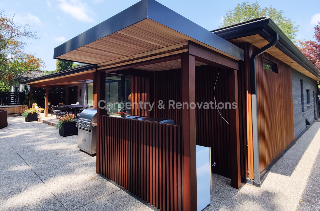 Modern outdoor kitchen and covered patio featuring custom wood slat design, black trim accents, and built-in grill — exterior craftsmanship by JB Carpentry & Renovations.