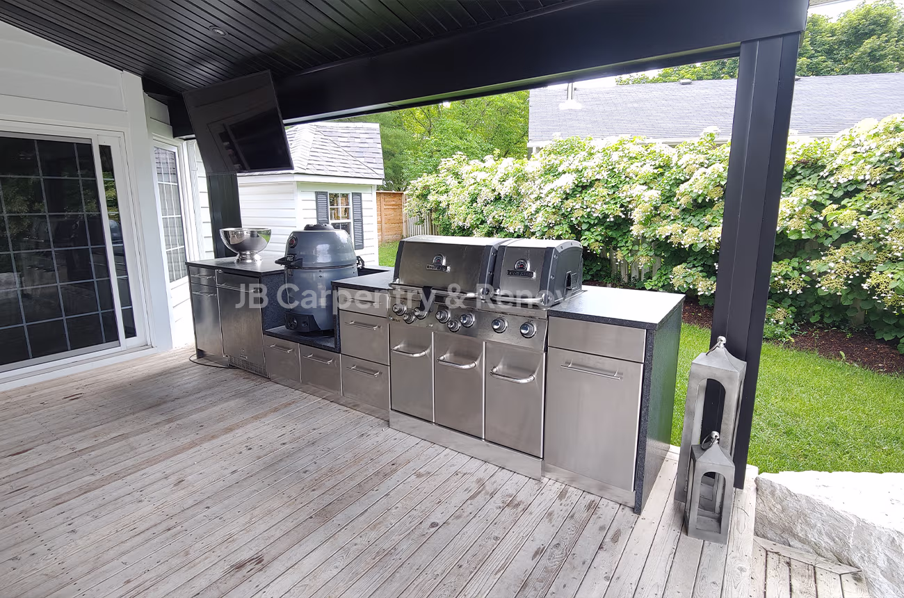 Custom outdoor kitchen with built-in stainless steel grills and cabinetry under a covered patio — exterior renovation by JB Carpentry & Renovations.