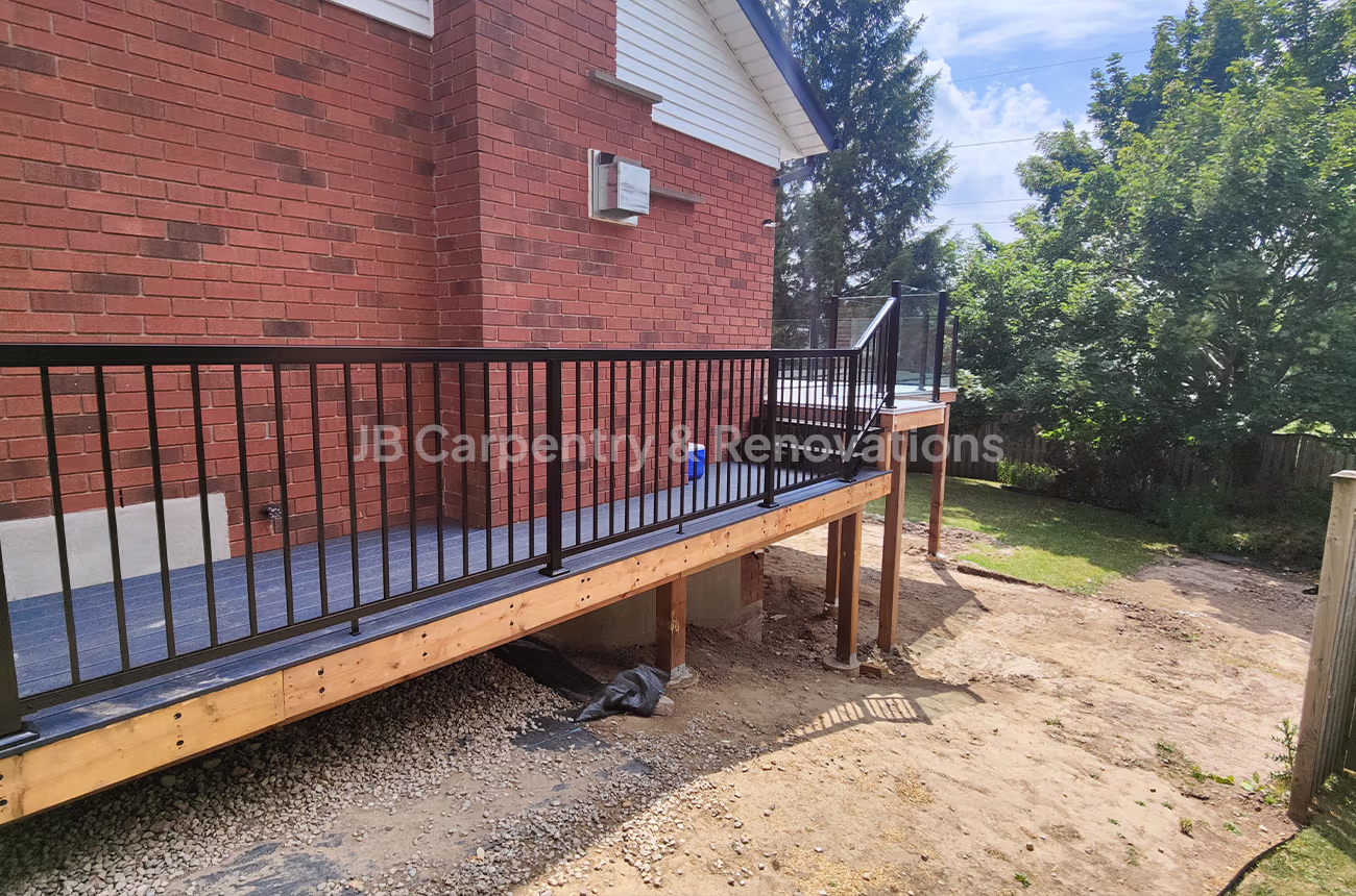 Custom-built elevated deck with black metal railing and composite flooring attached to a brick home — exterior renovation by JB Carpentry & Renovations.