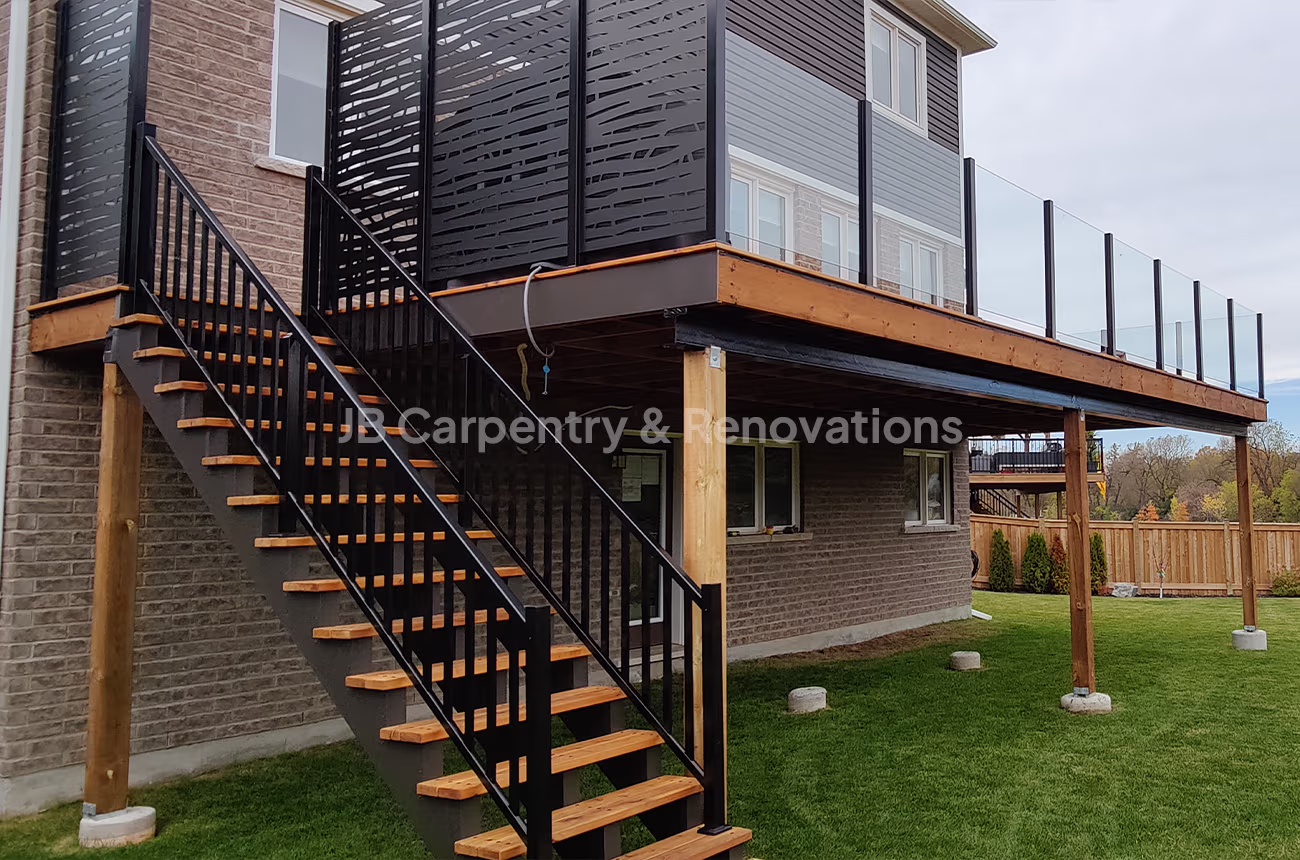 Elevated backyard deck with black privacy panels, glass railing, and custom wood staircase — designed and built by JB Carpentry & Renovations.