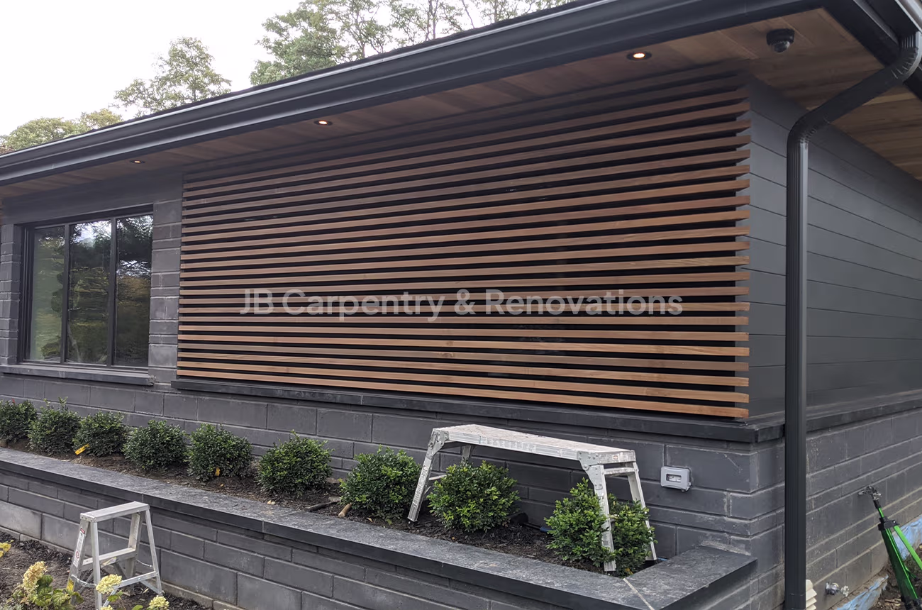 Modern horizontal wood slat exterior accent wall on black facade with integrated lighting — exterior renovation by JB Carpentry & Renovations.