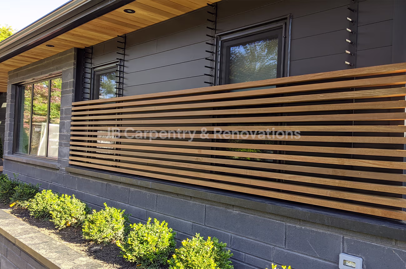 Custom horizontal wood slat exterior accent wall on dark modern home facade — detailed craftsmanship by JB Carpentry & Renovations.