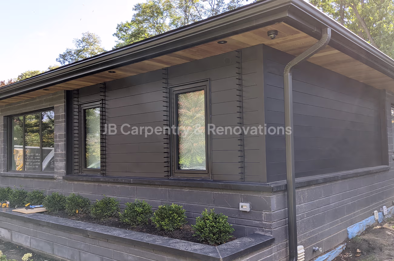 Sleek black exterior renovation with modern siding, detailed trim, and soffit lighting — professional exterior finish by JB Carpentry & Renovations.