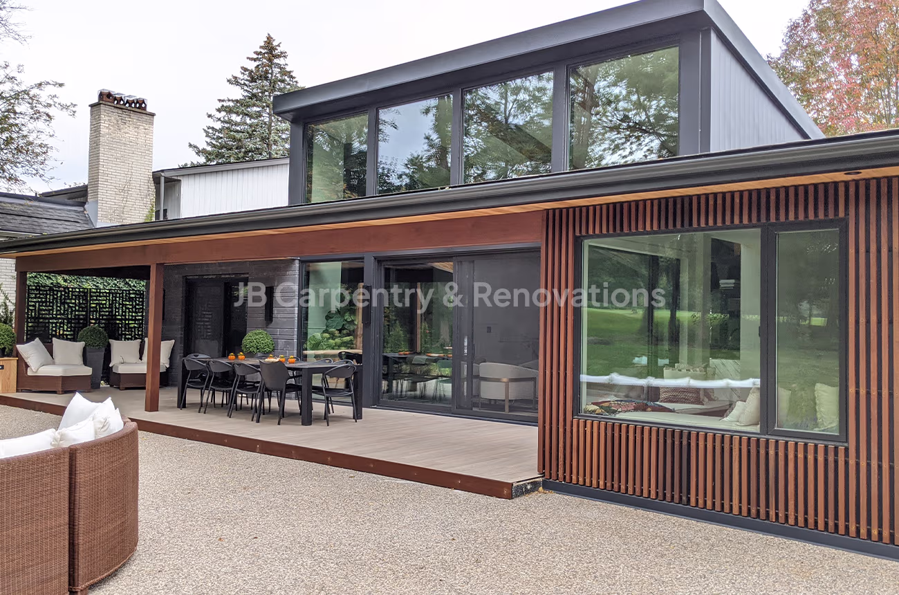 Contemporary home exterior featuring glass walls, natural wood siding, and a custom-built covered deck — full renovation by JB Carpentry & Renovations.