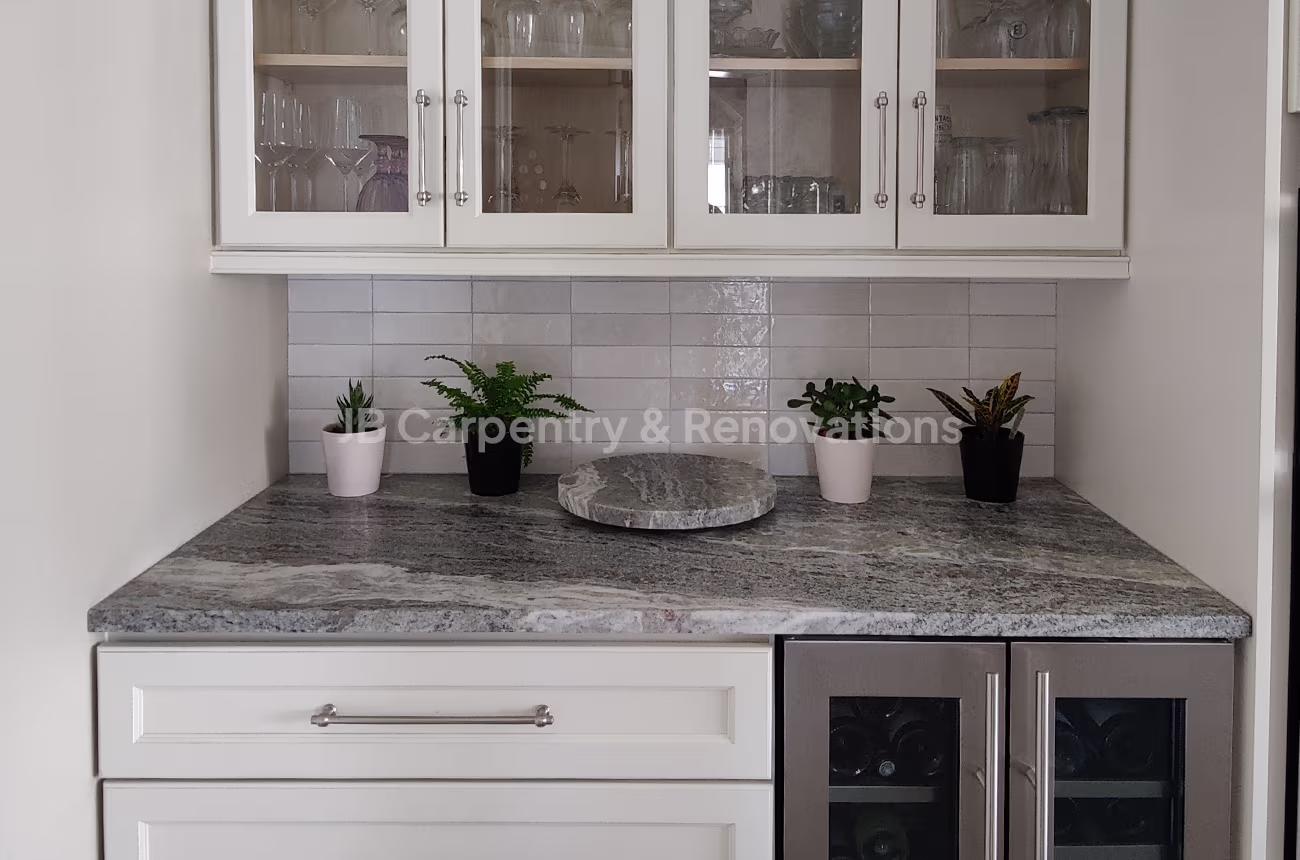 Built-in bar with glass upper cabinets, natural stone countertop, and under-counter wine cooler — JB Carpentry & Renovations.