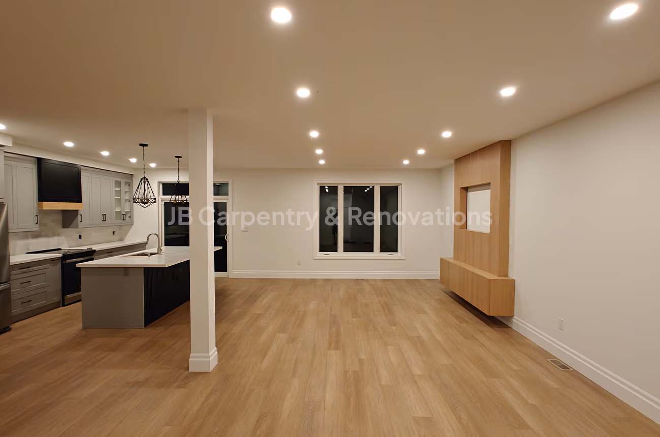 Open concept kitchen and living space with light wood floors – Spacious interior with recessed lighting, modern kitchen cabinetry, and a custom wood feature wall.