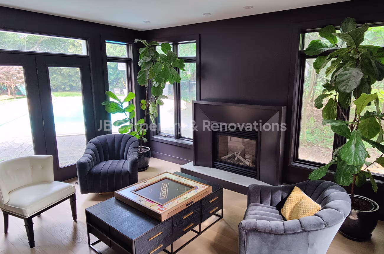 Dark modern living room with custom fireplace – Stylish lounge featuring dark-painted walls, custom fireplace surround, and large windows overlooking the backyard.