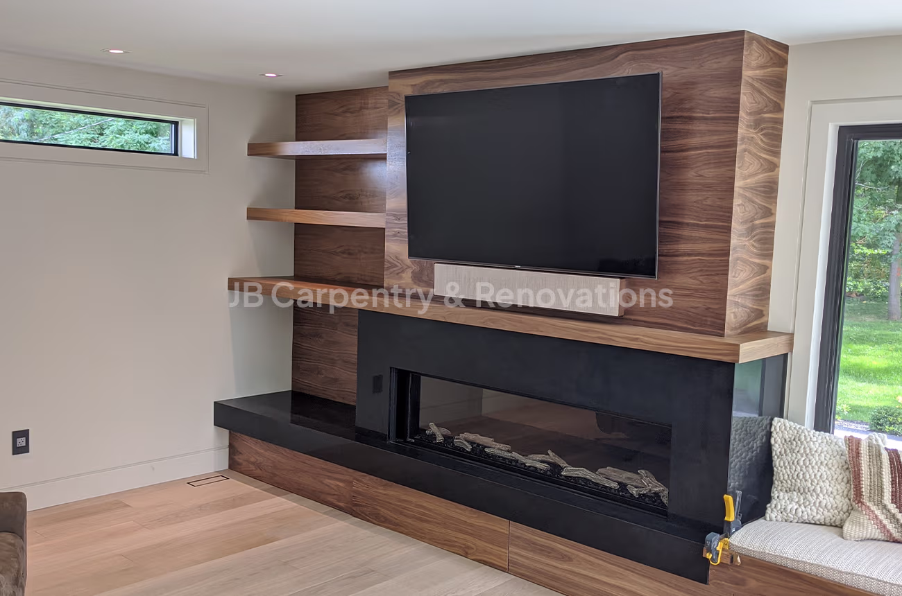Contemporary walnut fireplace wall with TV and shelving – Modern media wall featuring walnut wood panels, floating corner shelves, and a sleek black fireplace surround.