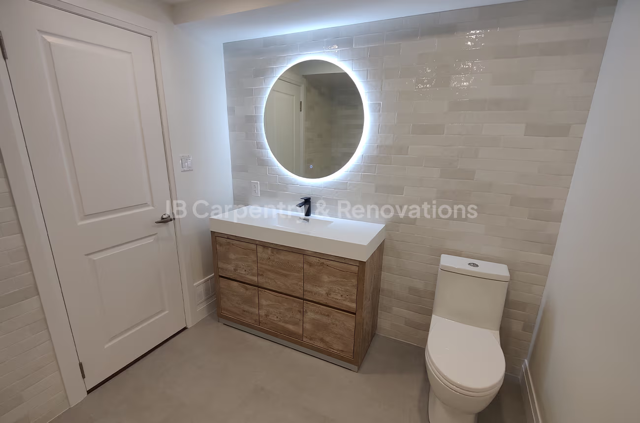 Bathroom with illuminated round mirror and light wood vanity – Scandinavian-inspired bathroom with floating vanity, backlit circular mirror, and neutral tiles.