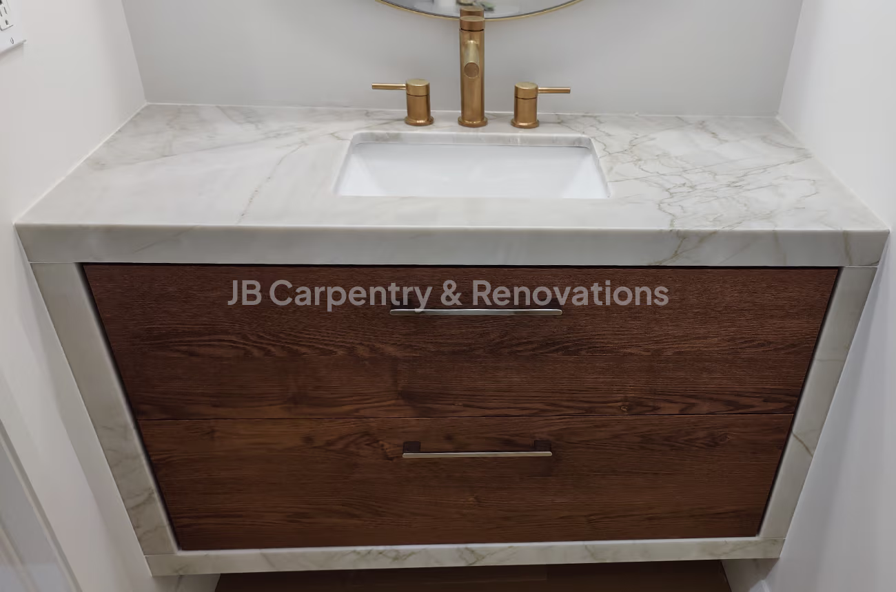 Wood and marble vanity with gold faucet – Compact vanity with marble top, gold faucet, and rich walnut drawers against a white wall.