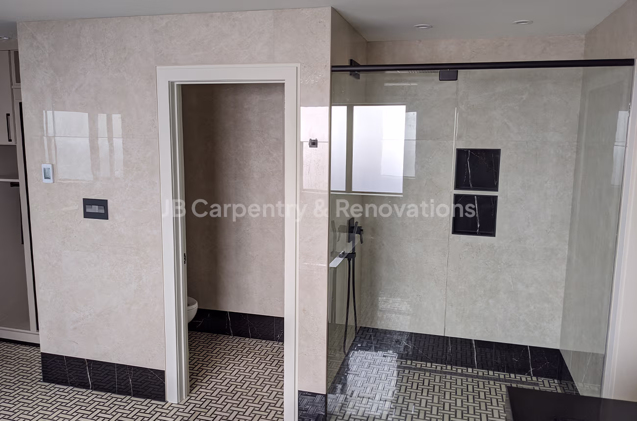 Large beige bathroom with black tile accents and walk-in shower – Spacious bathroom with neutral wall tiles, geometric black-and-white floor, and glass shower.