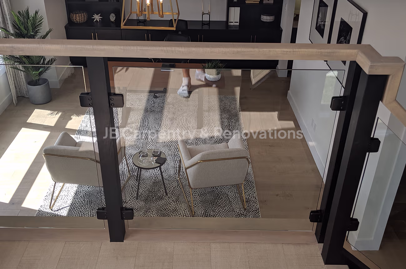 Glass railing overlooking modern living space – Sleek glass guardrail with wood cap and black hardware overlooking a bright living area.