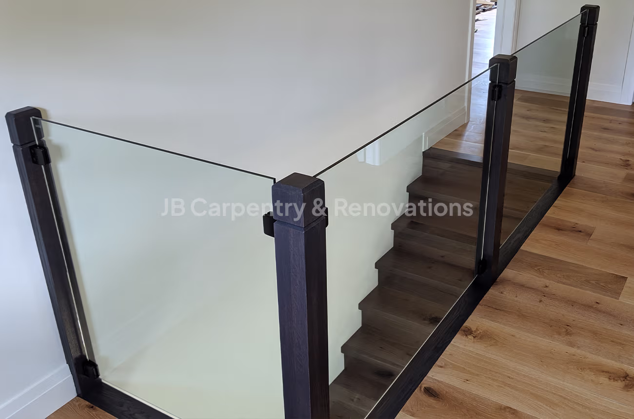 Modern staircase with black wood and glass railing – Minimalist staircase featuring dark-stained posts, clear glass panels, and wood flooring.