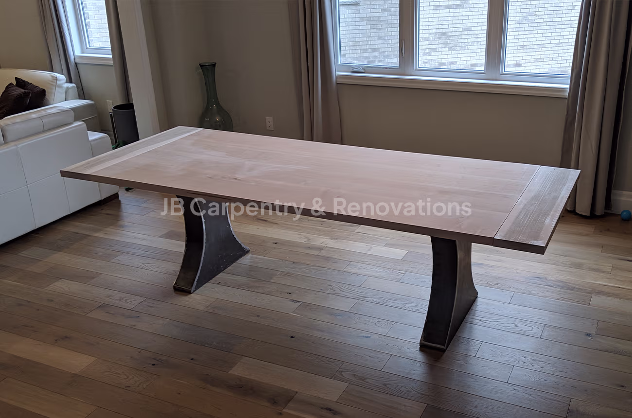 Light wood dining table on curved steel legs – Custom dining table with pale hardwood top and sculpted black metal pedestal legs.