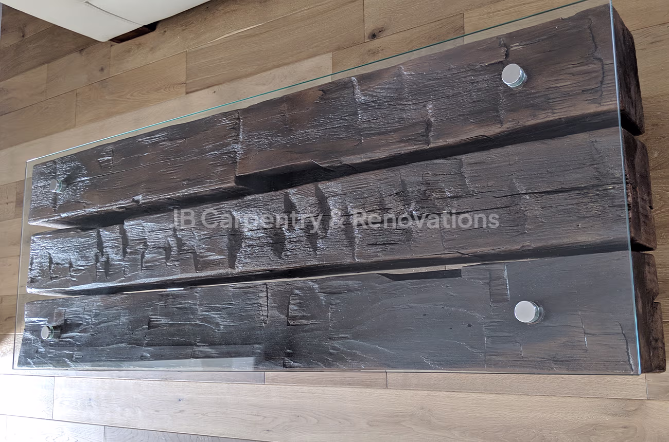 Reclaimed wood coffee table with glass top – Overhead view of a rustic coffee table made from dark reclaimed wood beams with a sleek glass surface and metal hardware.