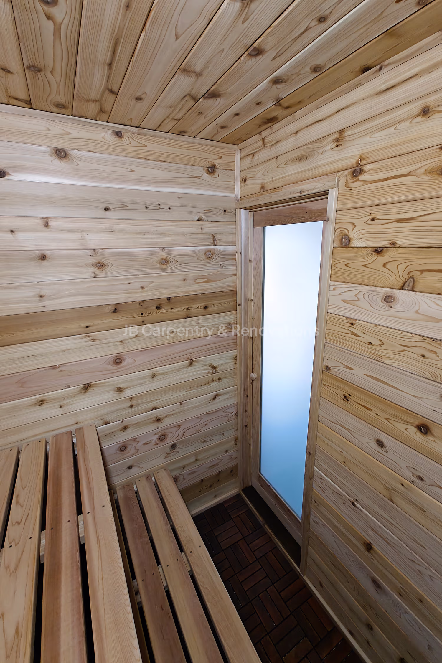 Custom cedar sauna with bench seating and frosted glass door – Handcrafted wood sauna interior featuring tongue-and-groove cedar paneling and built-in bench design.