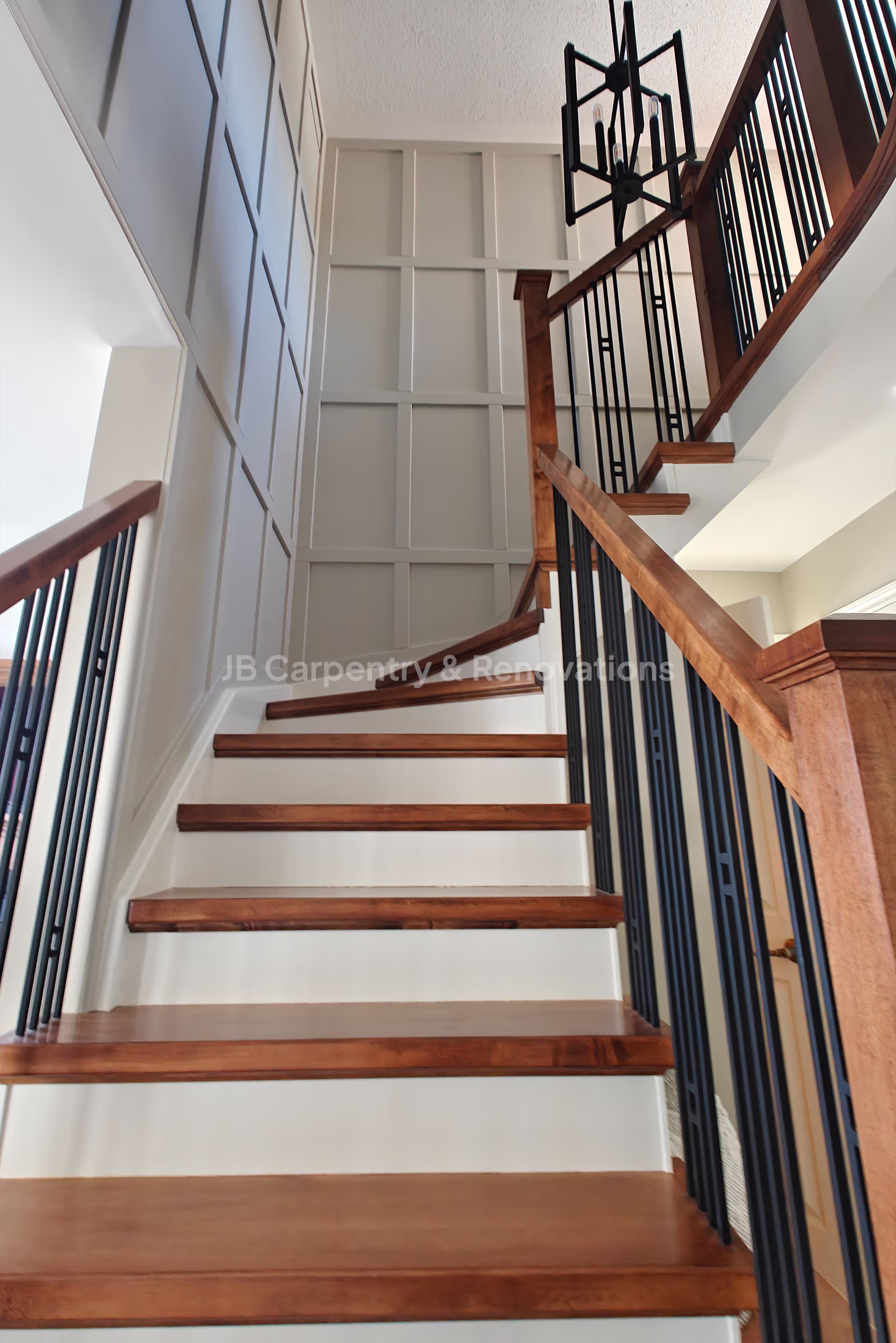 Wood staircase with metal balusters and feature wall paneling – Contemporary staircase design combining wood treads, black metal spindles, and detailed wall trim.