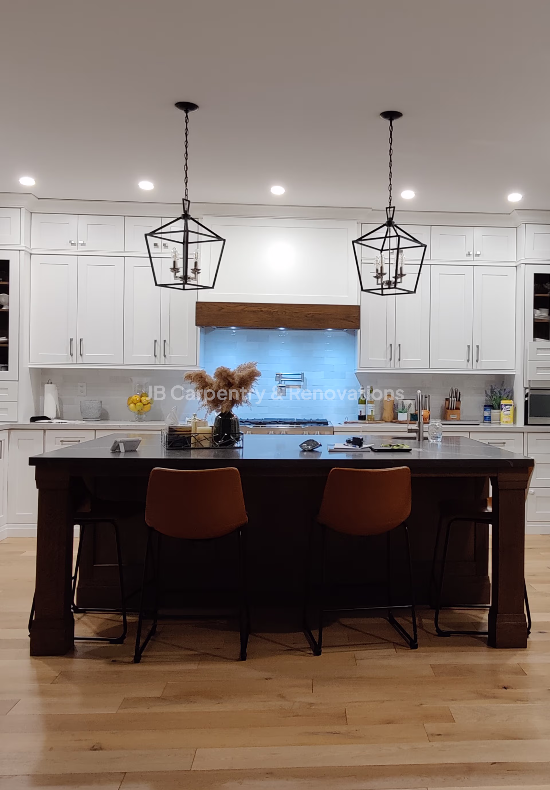 Classic white kitchen with large island and pendant lighting – Elegant kitchen renovation with shaker-style cabinetry, black accents, and wood flooring.