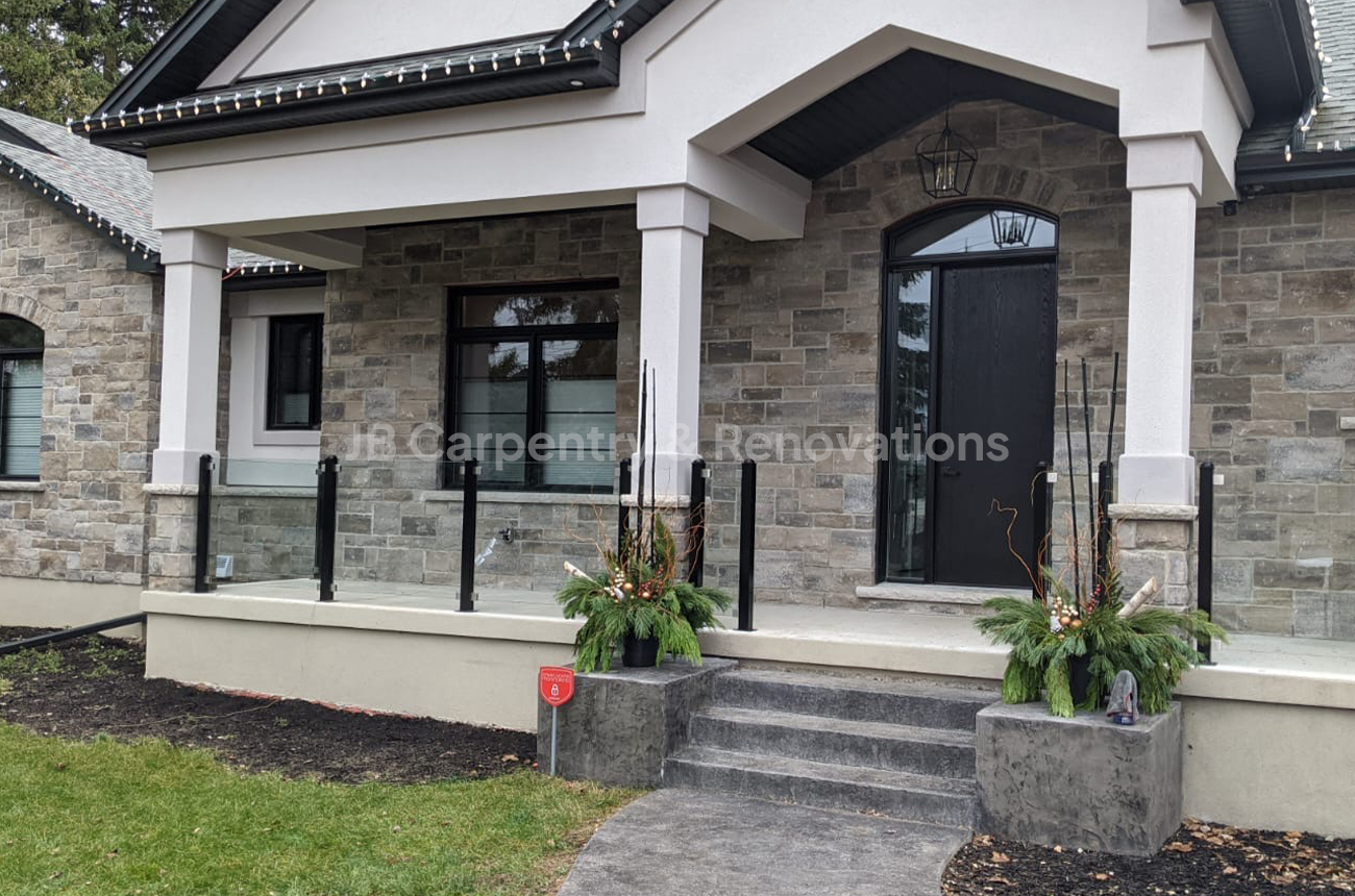 Custom new build with stone columns and glass porch railing – Refined entrance design featuring natural stone, white trim, and sleek glass railing details.