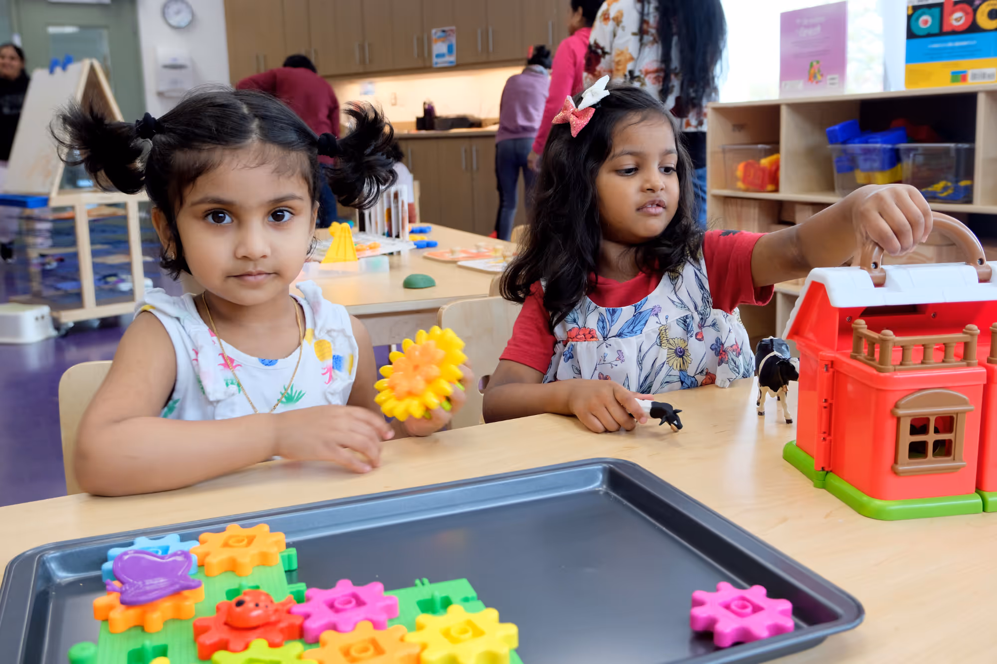 Two young girls playing with colorful toys at a classroom table.