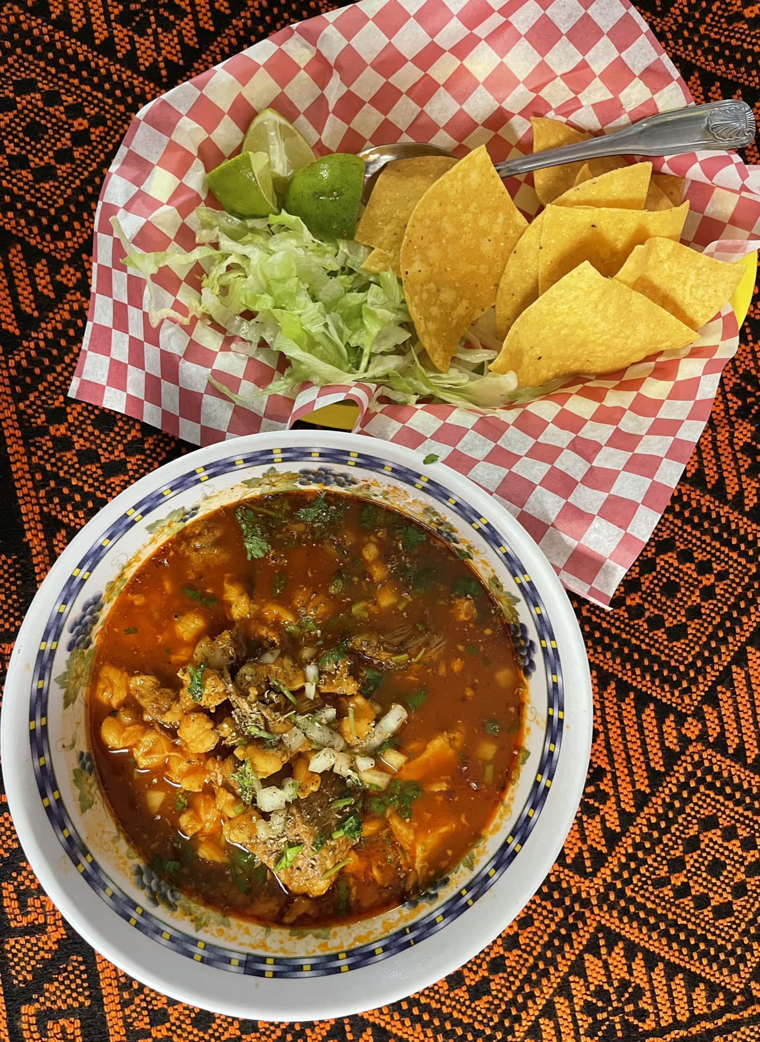 A steaming bowl of pozole filled with vegetables and herbs, placed on a wooden table.