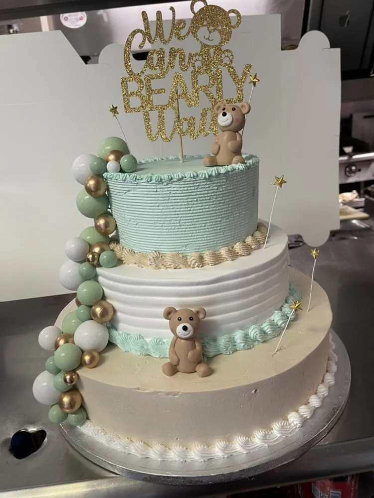 A three-tiered cake topped with strawberries and a cute teddy bear figurine on top.