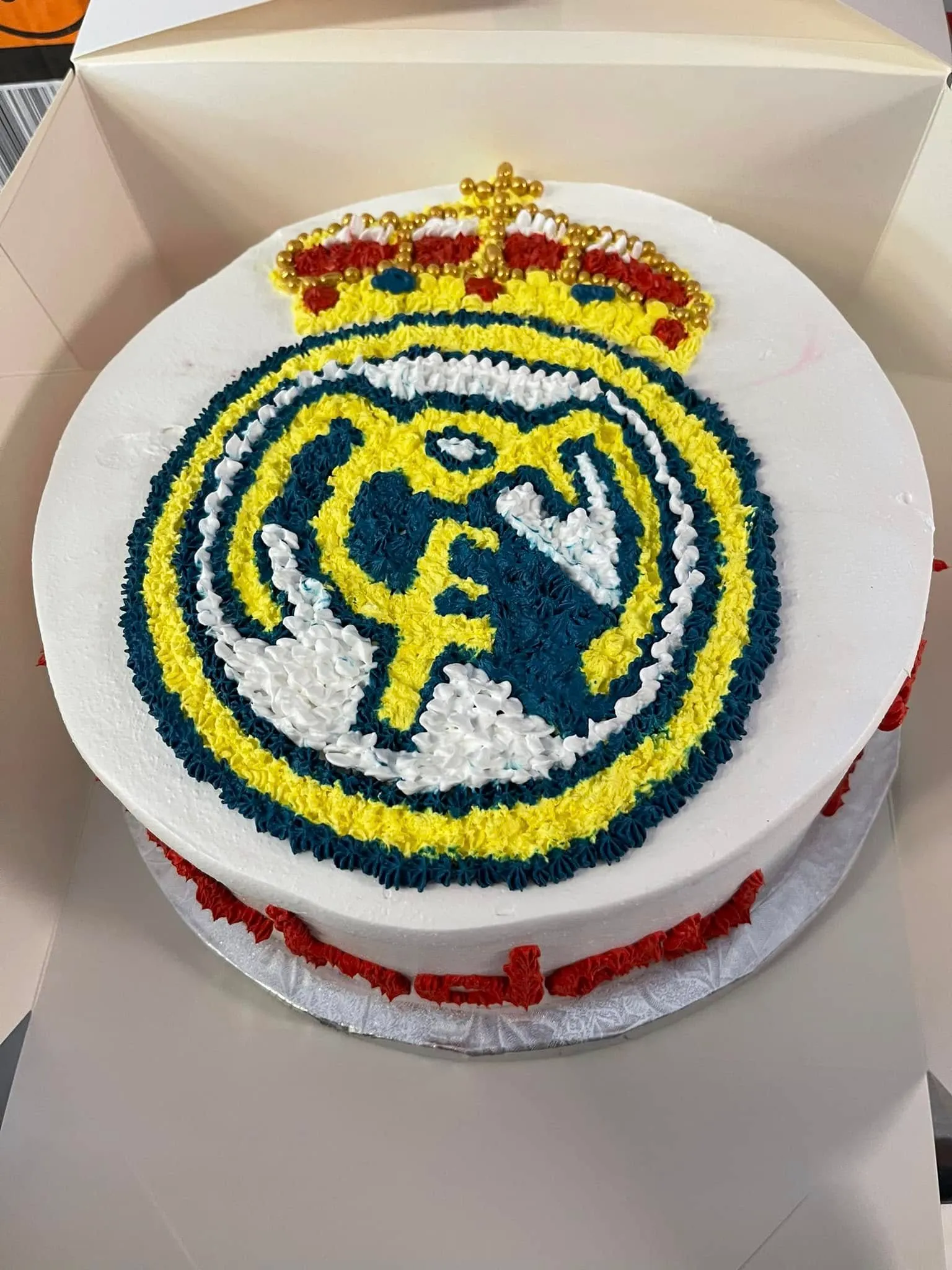 A cake decorated with the Real Madrid logo, featuring white frosting and the team's iconic colors.