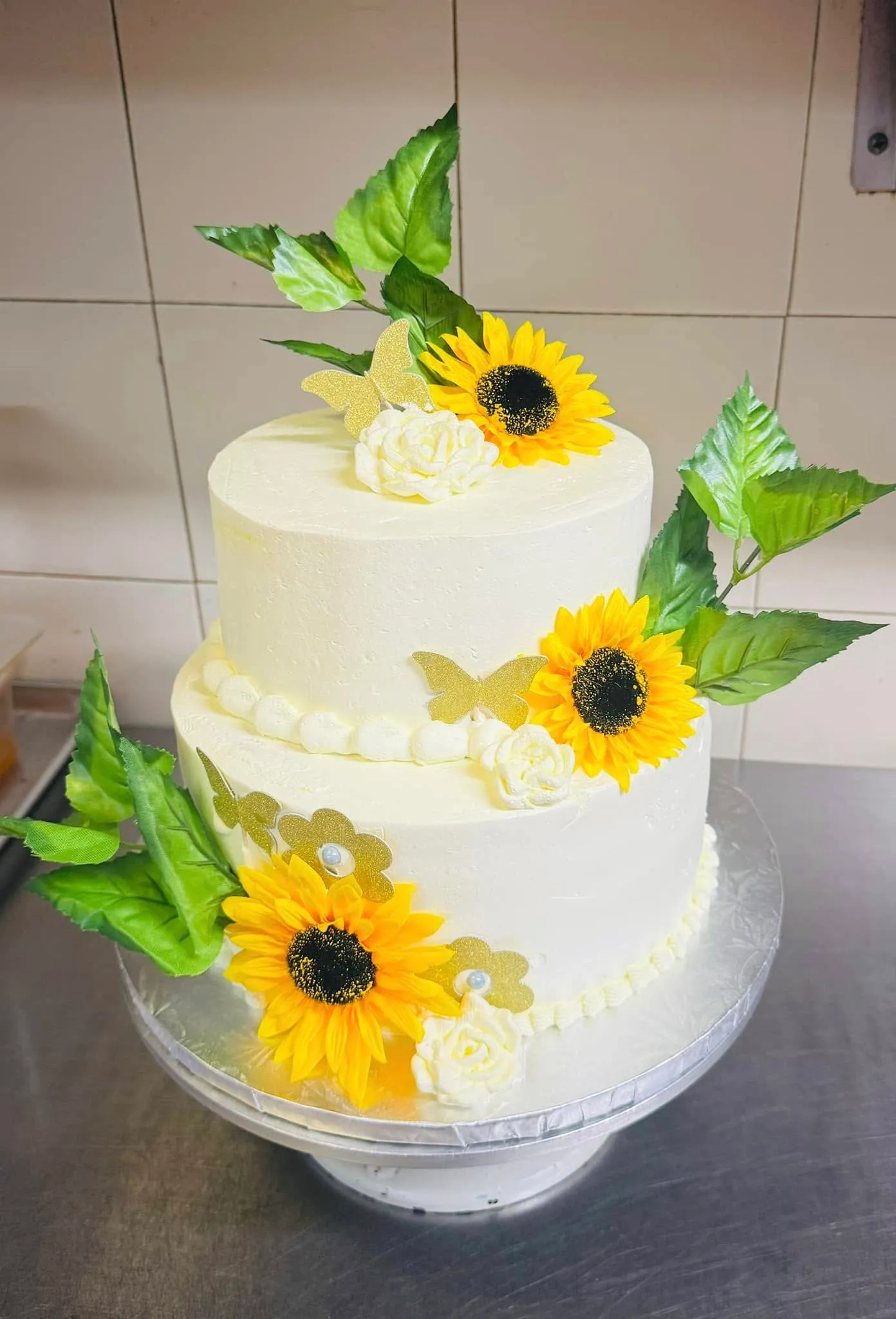 A white cake adorned with vibrant sunflowers and green leaves on top, creating a cheerful and elegant presentation.