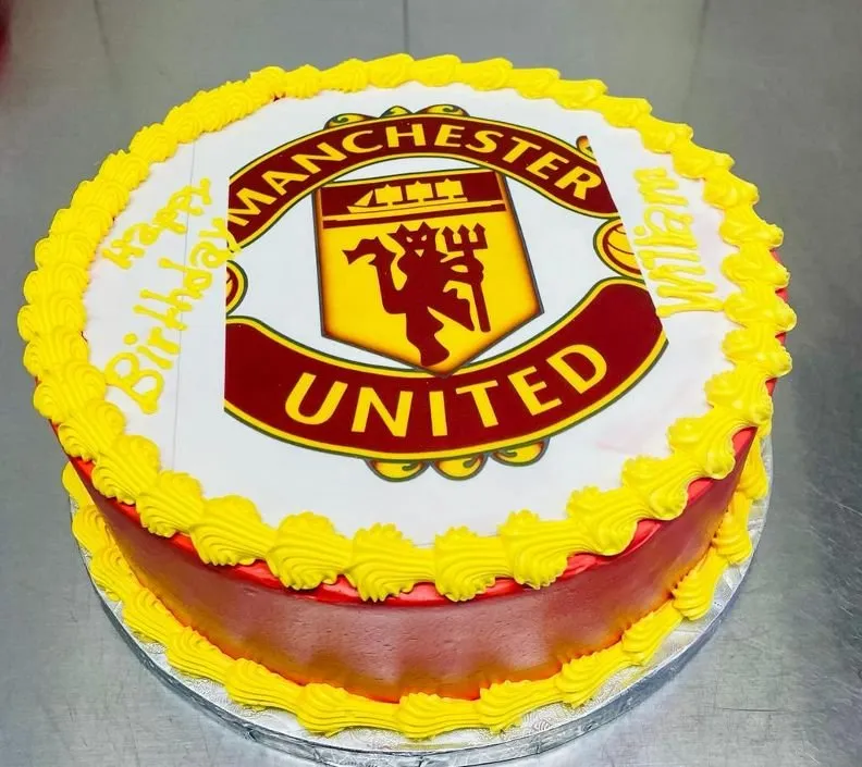 A cake featuring the Manchester United logo, beautifully topped with ripe strawberries.