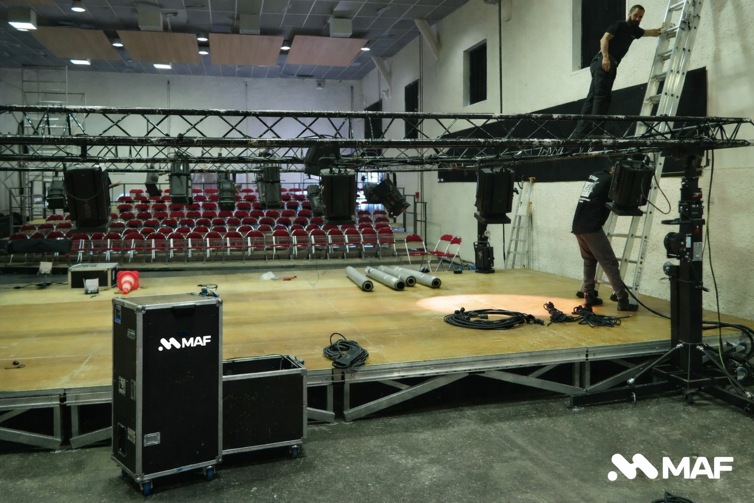 Des techniciens installent des équipements de scène, y compris des éclairages et une structure en treillis, dans une salle de spectacle.