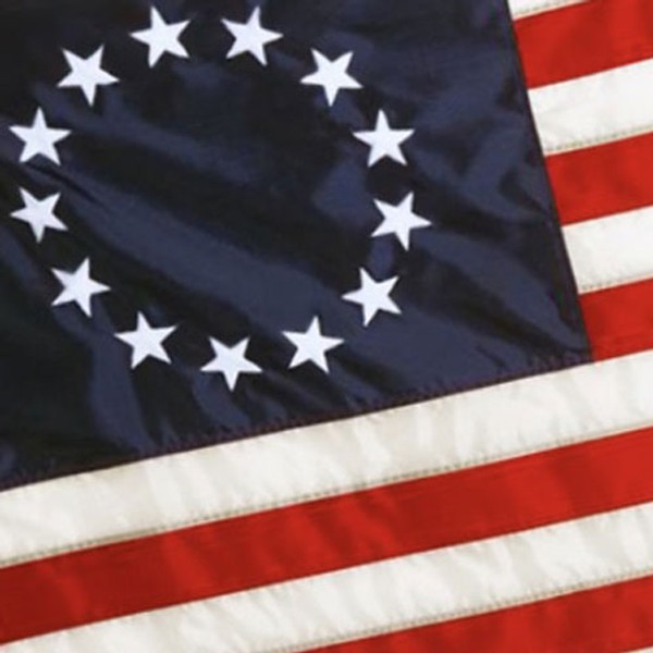 Close-up of the Betsy Ross American flag showing 13 white stars in a circle on a blue field over red and white stripes.
