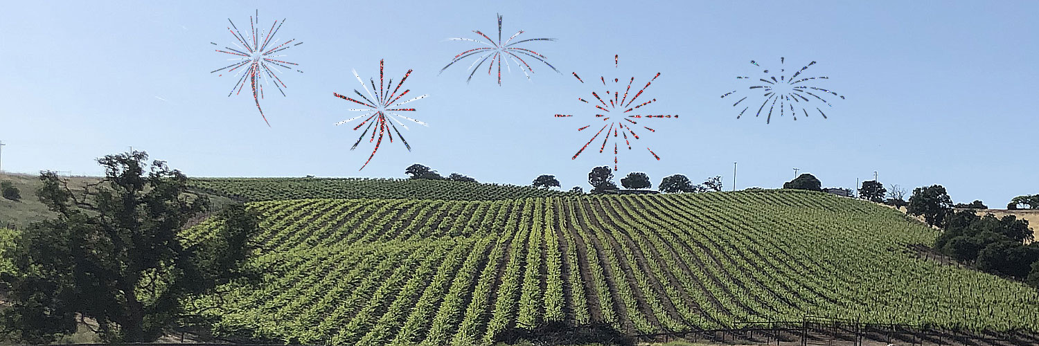 Faux Fireworks exploding above a green vineyard under a clear blue sky.