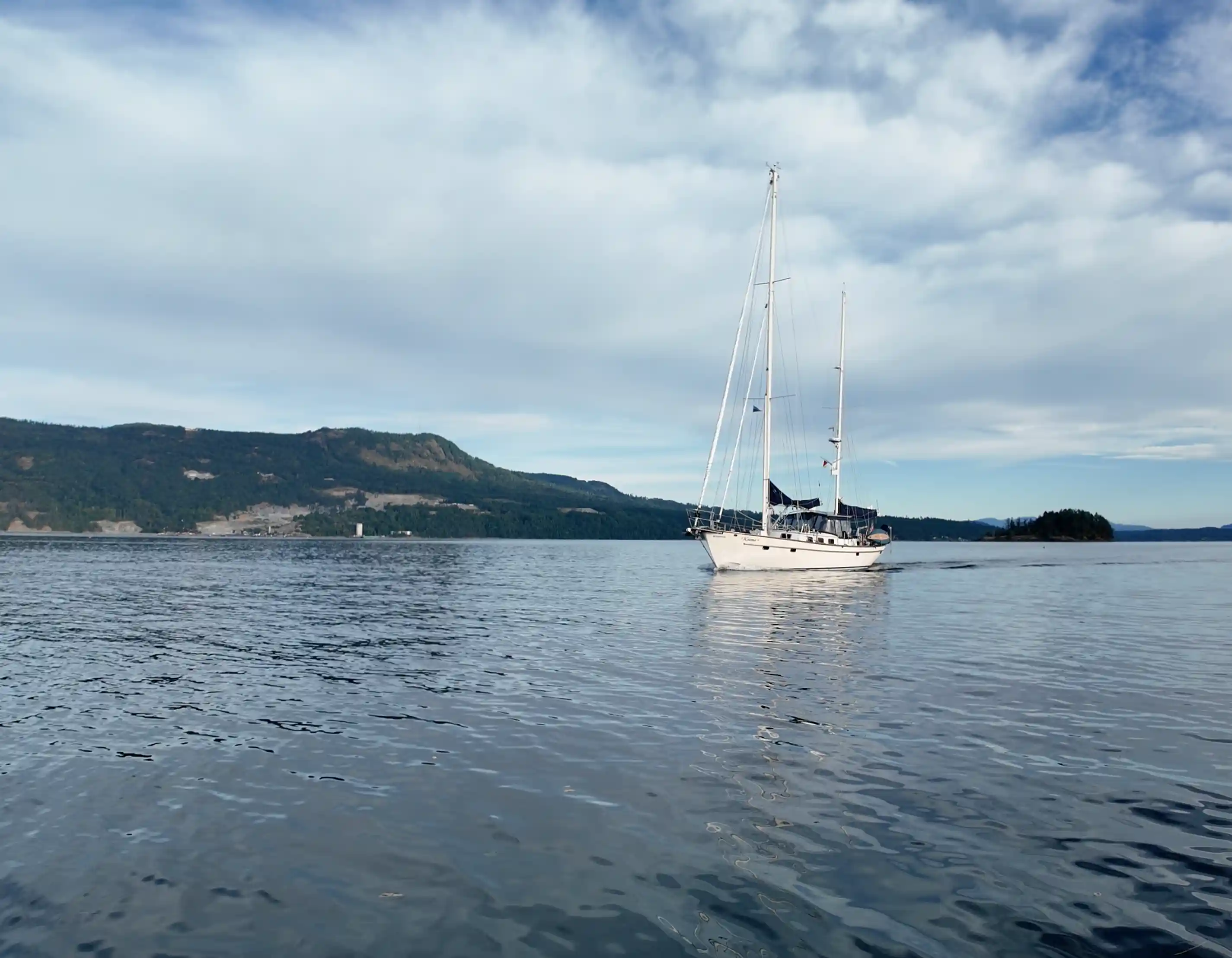 Sailboat floating on calm water with mountains in the background under a cloudy sky