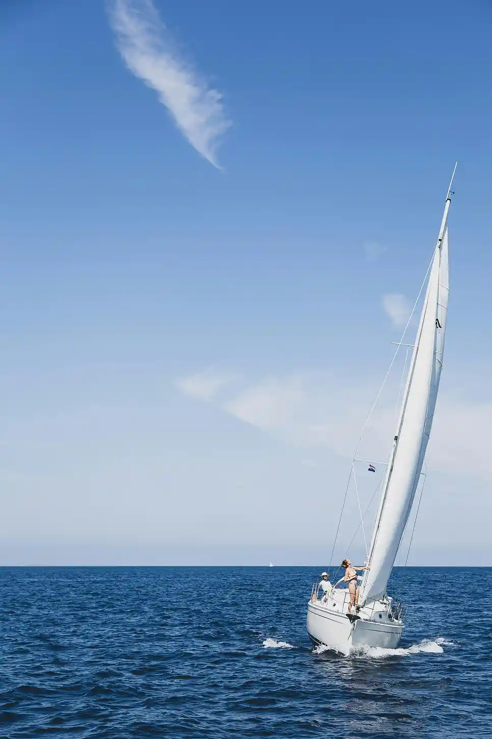 Sailboat with two people cruising on the open sea.