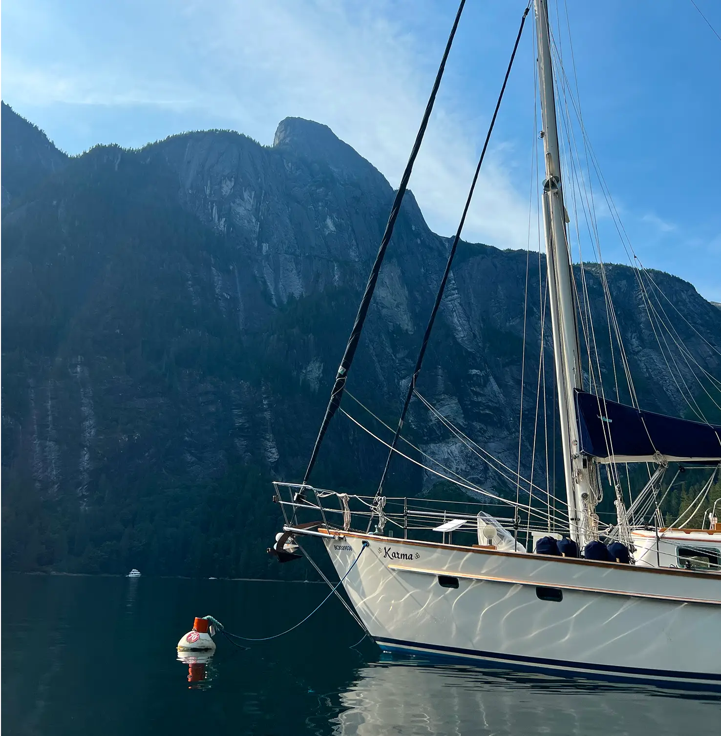 Sailboat named “Karma” anchored on calm water with steep forested mountains in the background.