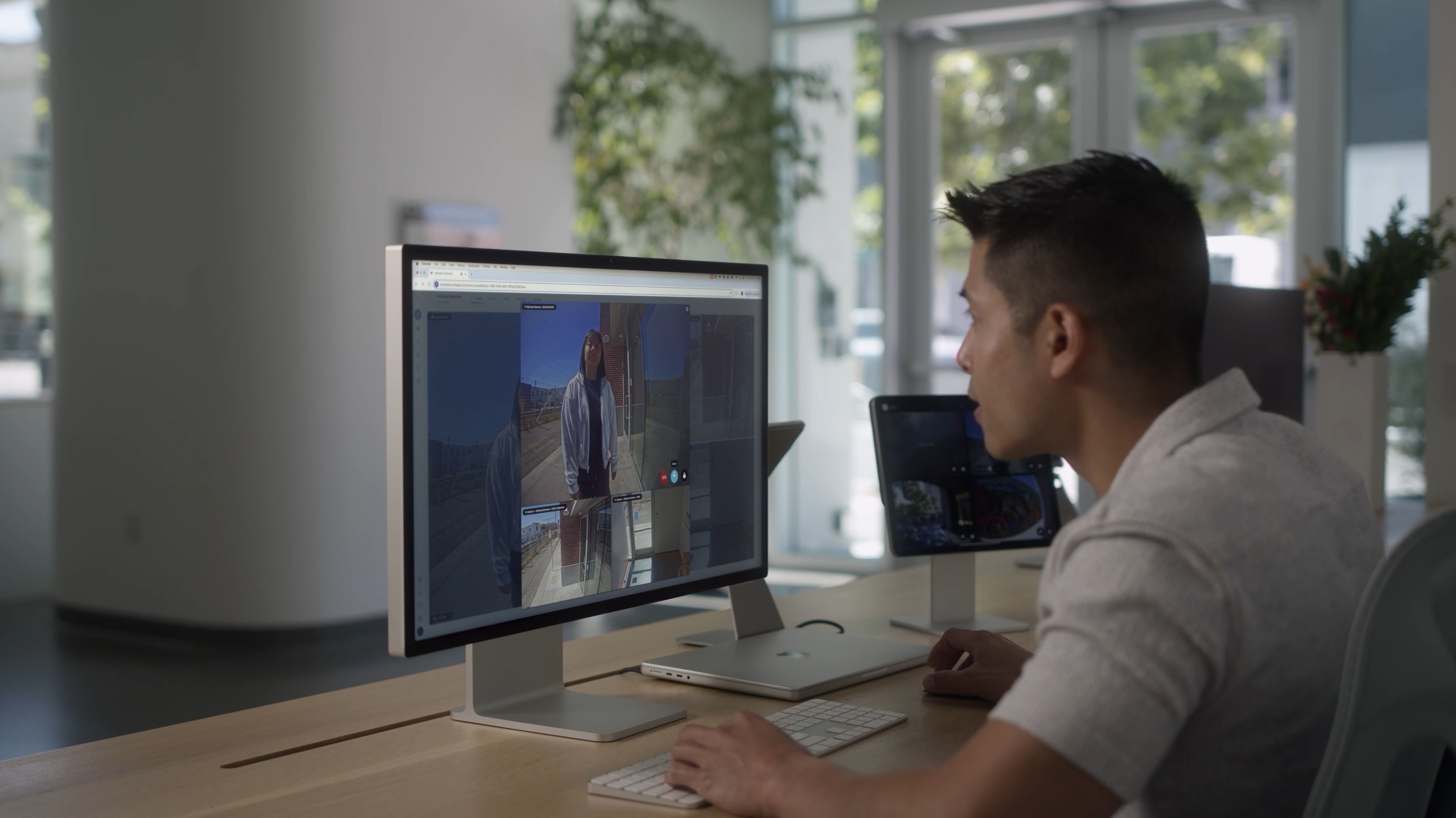 Man sitting at a desk looking at a computer screen showing a video call with a woman standing outside a building.