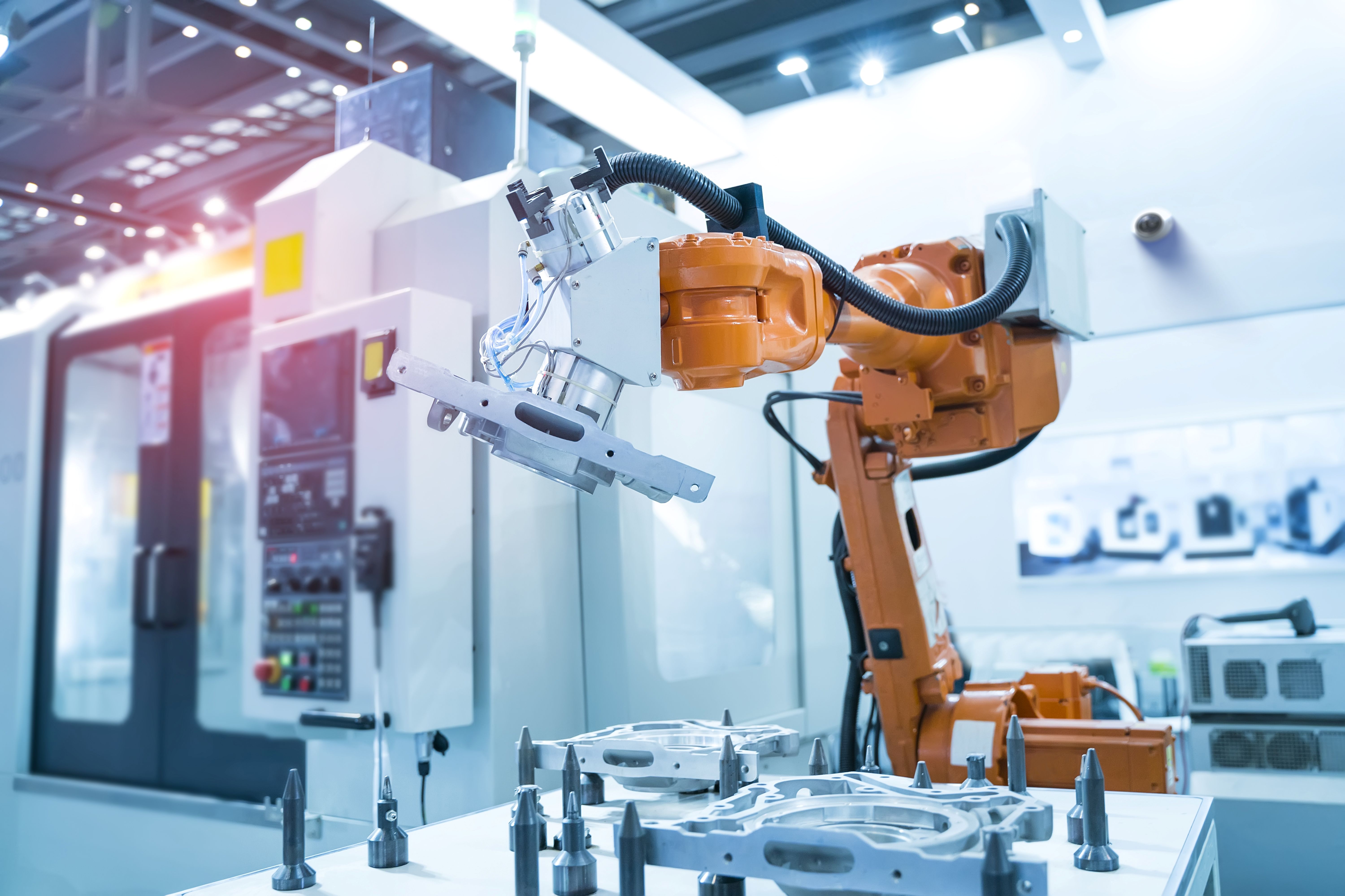Orange industrial robotic arm handling metal parts inside a modern manufacturing facility.