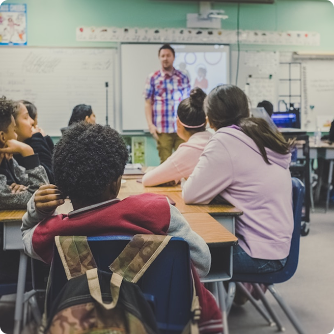Students at their desks in class listening to a teacher