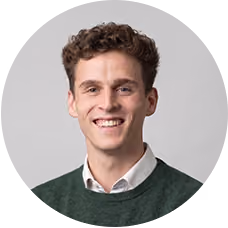 Smiling young man with curly brown hair wearing a green sweater and white collared shirt.