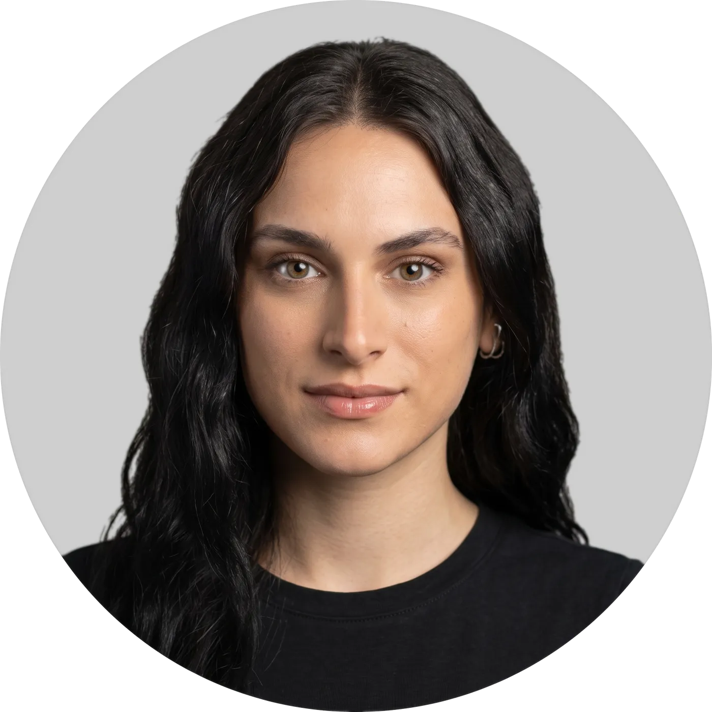 Circular headshot photo of a woman with long dark wavy hair, wearing a black top, on a gray background