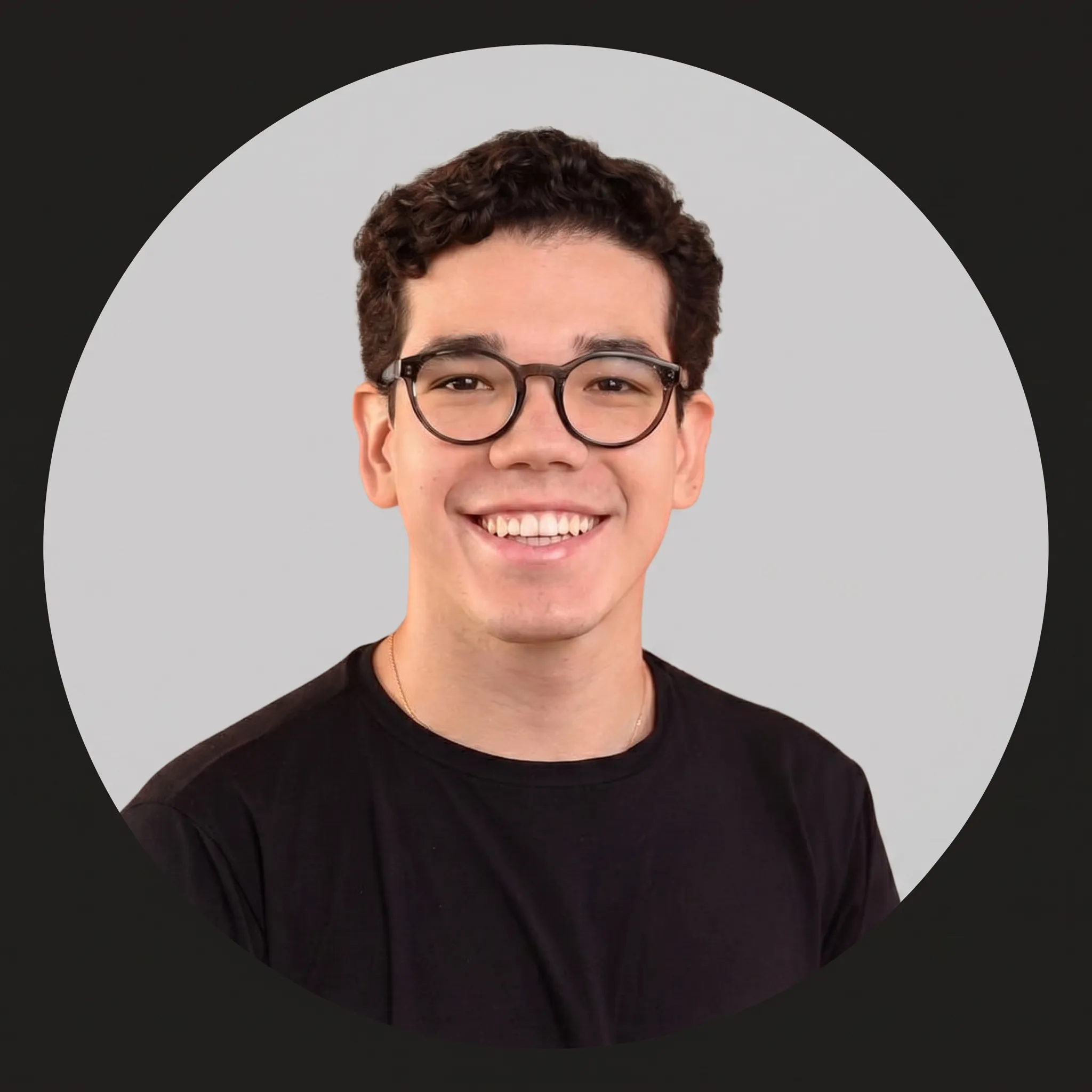 Photo of a smiling young man with curly hair and glasses, wearing a black t-shirt, against a plain gray circular background