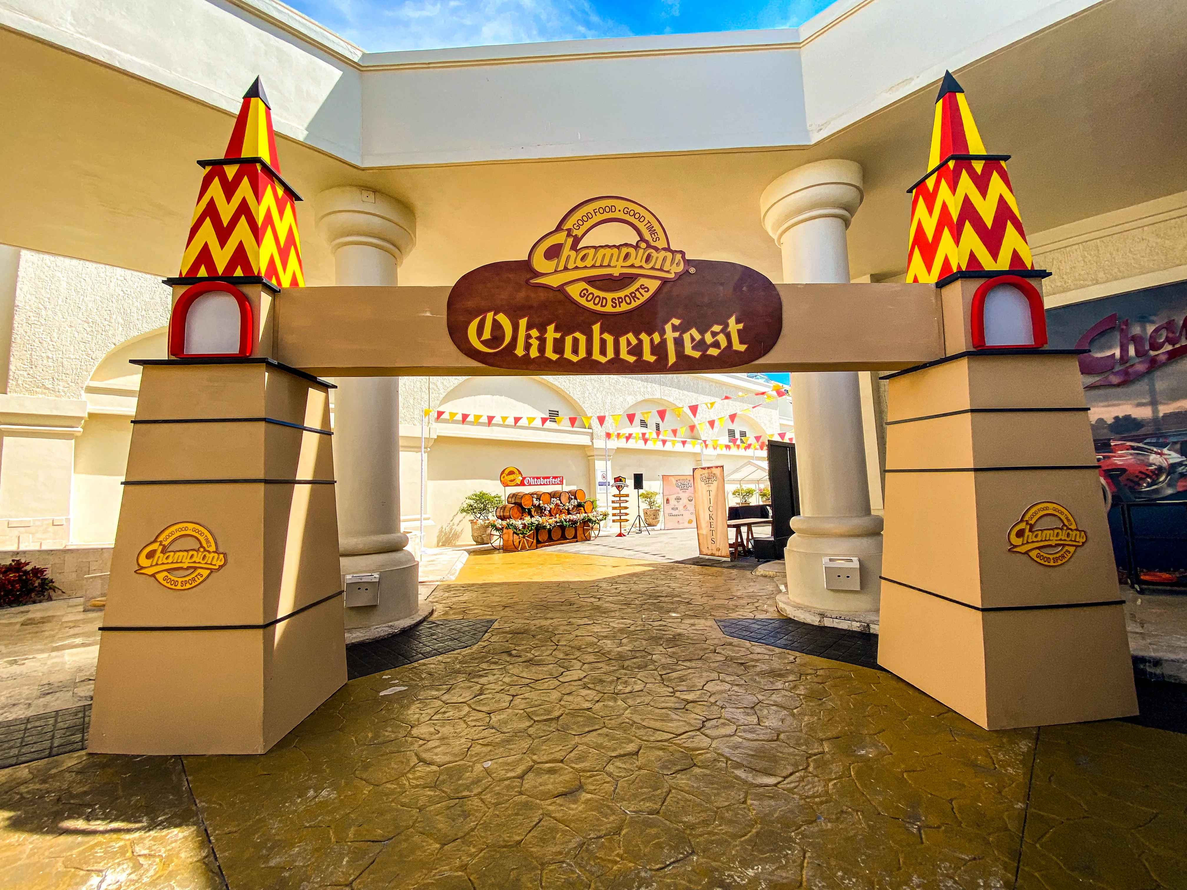 A red and yellow Bavarian-style marquee archway stands over a stone walkway outside a resort building.