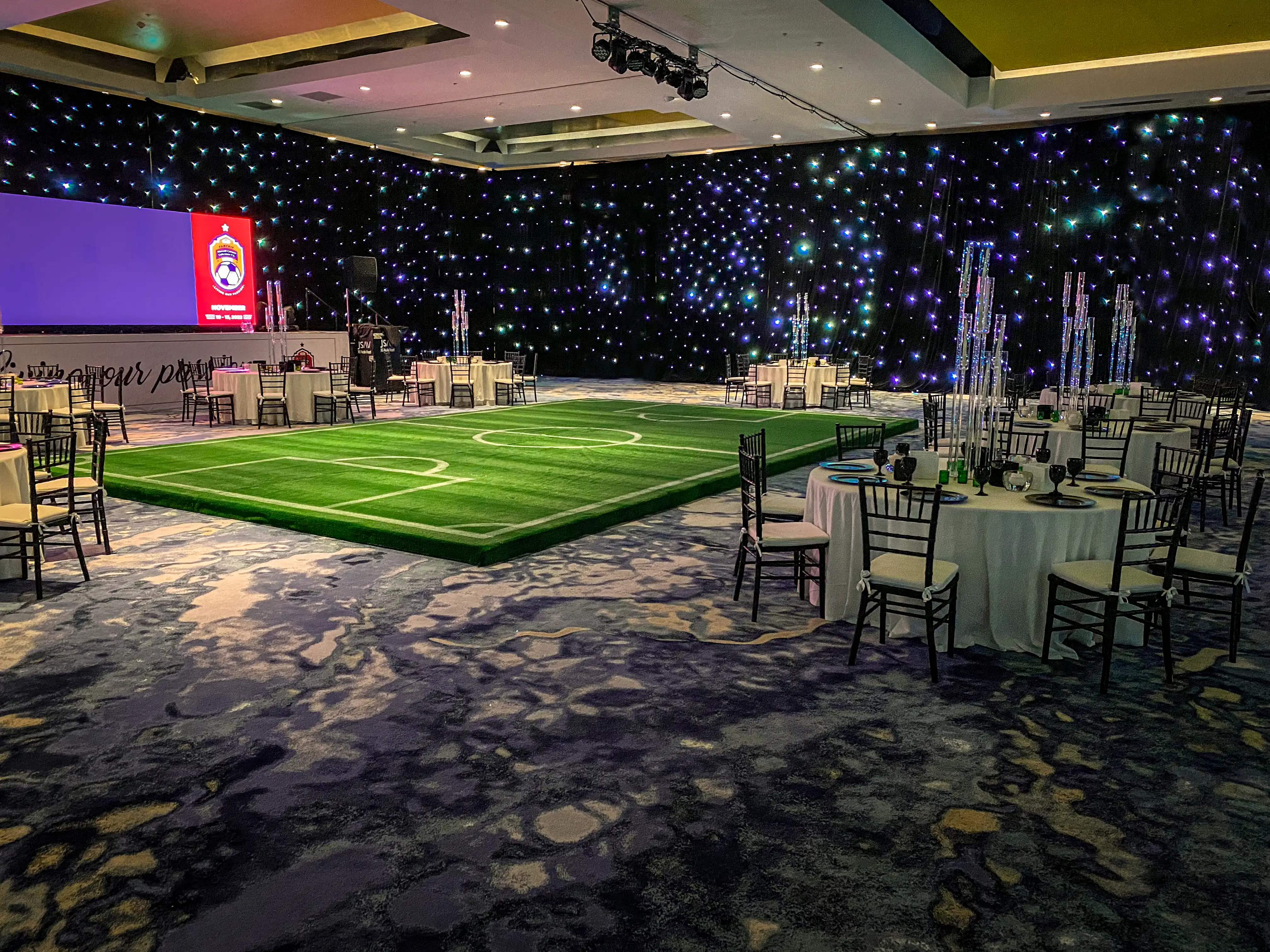 Completed gala dinner featuring a football pitch stage, banquet seating and large presentation screen.