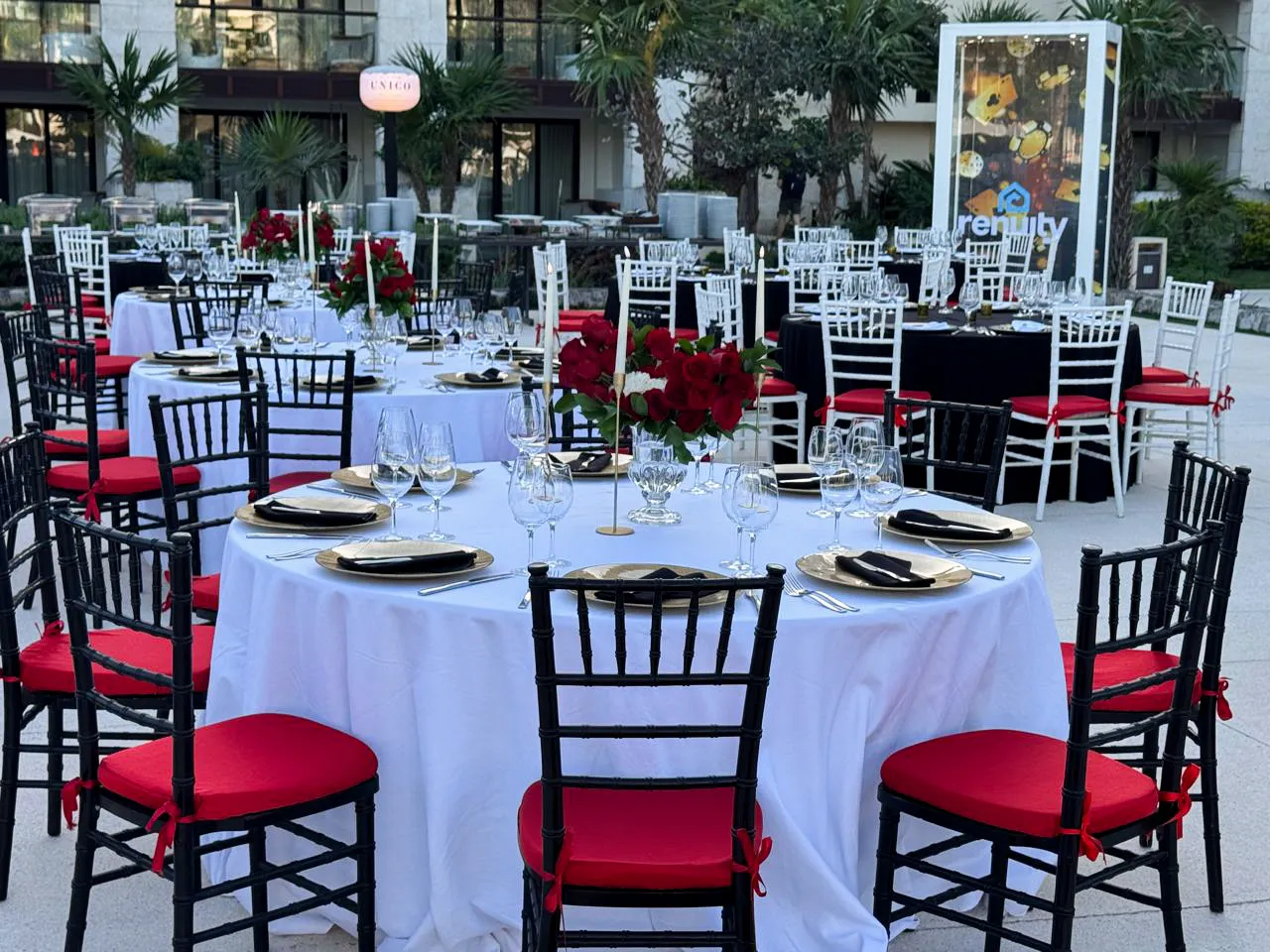 A white dinner table with black chairs, red cushions, gold chargers, and red flowers at the outdoor casino gala.