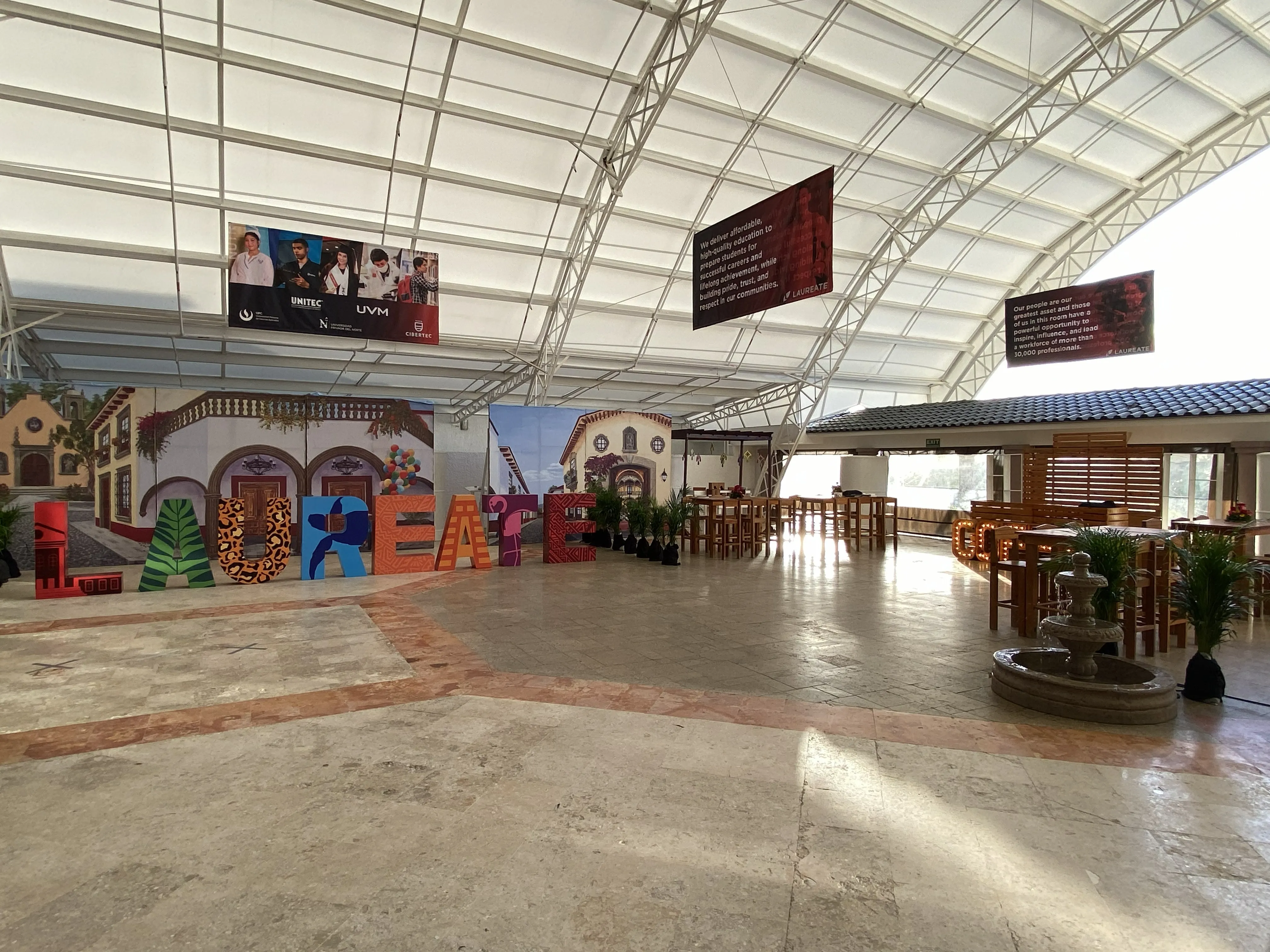 Covered meeting arrival area with a panoramic pueblo backdrop, colorful dimensional letters, hanging banners, and a coffee station.